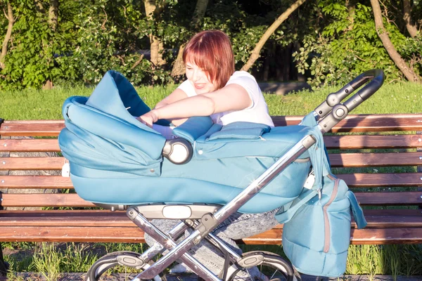 Mother sitting on a bench and talking with a child in a stroller — Stock Photo, Image