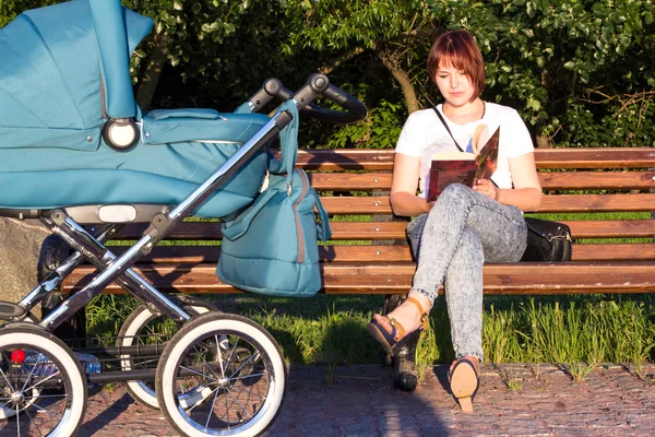 Annem onun Bebek arabasındaki bebek parktaki bir bankta bir kitap okuma