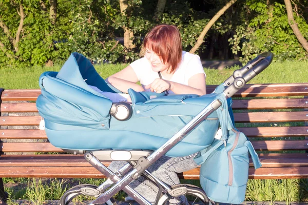 Moeder zittend op een bankje en praten met een kind in een kinderwagen Stockfoto