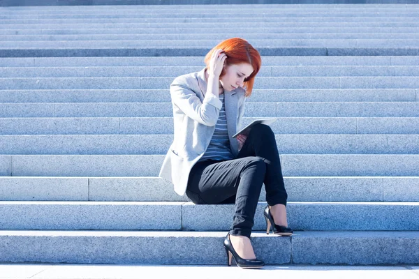 Mujer sentada en las escaleras en la calle y trabajando en una tableta —  Fotos de Stock