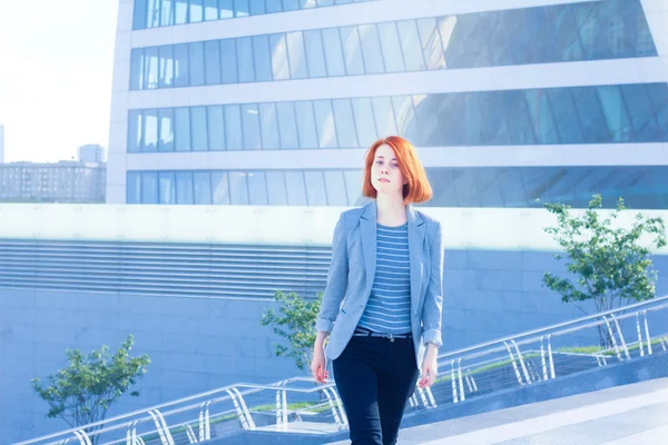 Redhead zakenvrouw de trap op de achtergrond van een wolkenkrabber — Stockfoto
