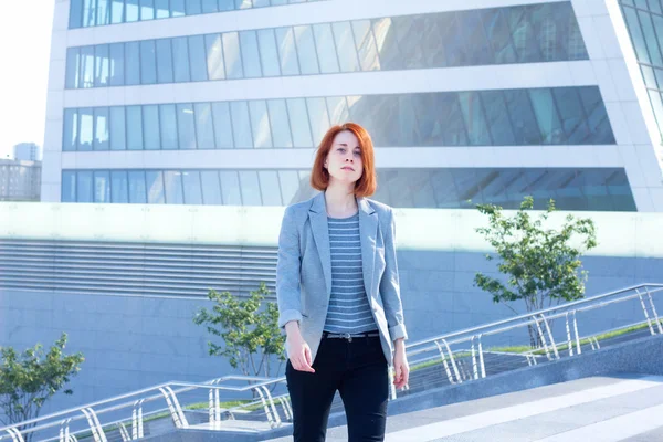 Redhead business woman up the stairs on the background of a skyscraper — Stock Photo, Image