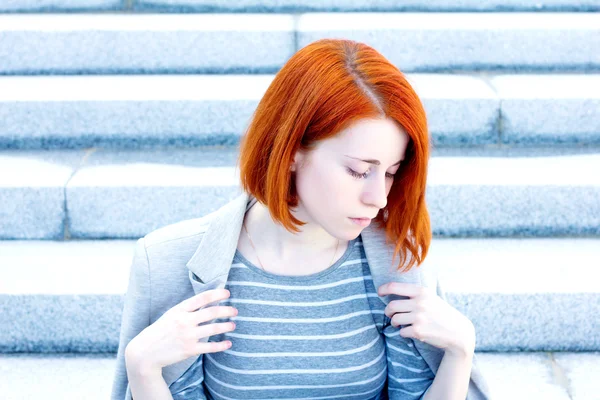 红发女郎美丽的年轻女子，与坐在楼梯上的一件夹克 — 图库照片
