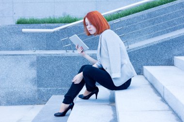 Güneşli bir günde bir tablet ile sokakta oturan iş kadın