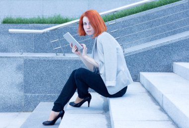 Kızıl saçlı çekici kadın dışında tablet ile merdivenlerde oturan