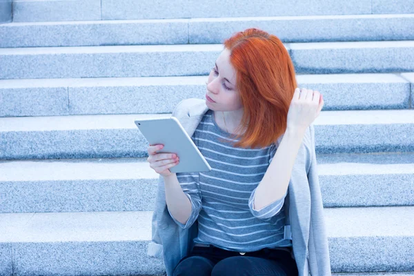 Vörös hajú nő ül a lépcsőn, megérintette a haját, és nézett tabletta — Stock Fotó