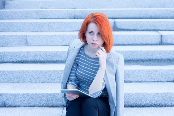 Redhead attractive woman sitting outside on the stairs with tablet