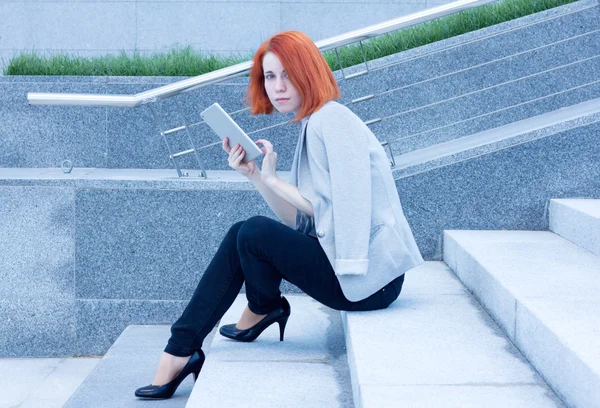 Pelirroja atractiva mujer sentada afuera en las escaleras con la tableta —  Fotos de Stock