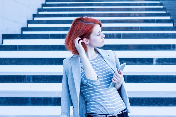Business woman with a tablet in hands looking aside on the background of the stairs in the business center — Stock Photo, Image