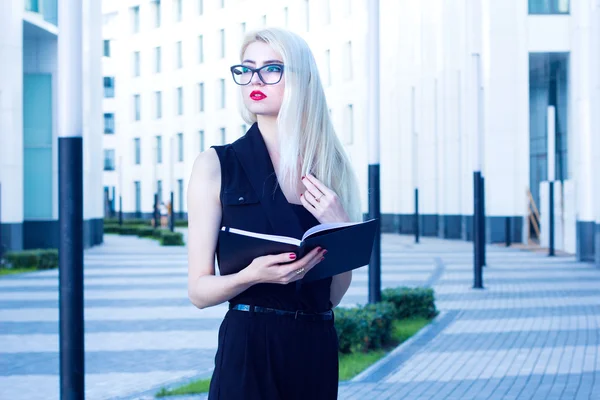 Mujer de negocios con un cuaderno mirando a la distancia en el fondo del centro de negocios —  Fotos de Stock