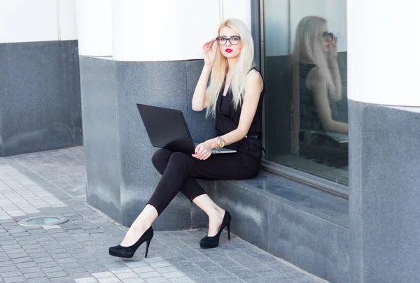 Biznes blond z czerwonymi ustami siedzi i praca z laptopem — Zdjęcie stockowe