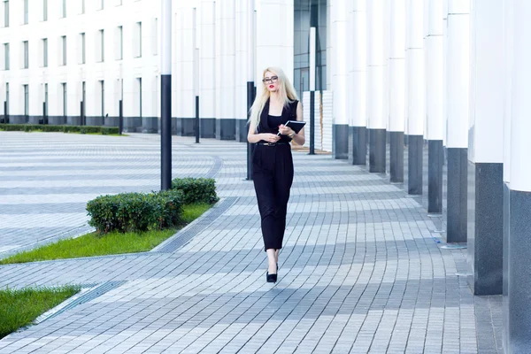 Donna intelligente con notebook cammina lungo la strada sullo sfondo del business center — Foto Stock