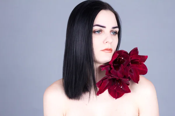美丽的黑发女郎，红的花，在她的肩上。美容治疗. — 图库照片