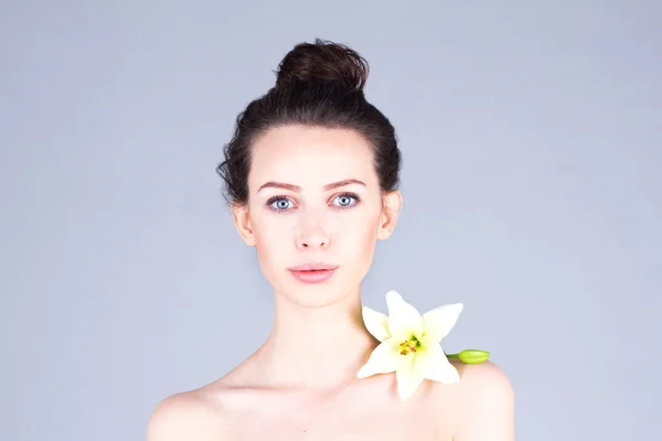 Beautiful woman with big eyes and clear skin. Woman with a flower on the shoulder.