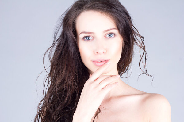 Beautiful young woman with big blue eyes and curly hair smiling and touching lips. Beautiful face of woman.