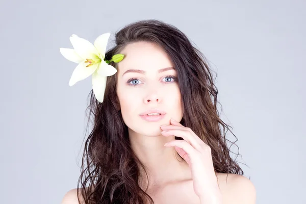 Woman with curly hair and big blue eyes touching lips. Woman with a flower in her hair. Stock Image