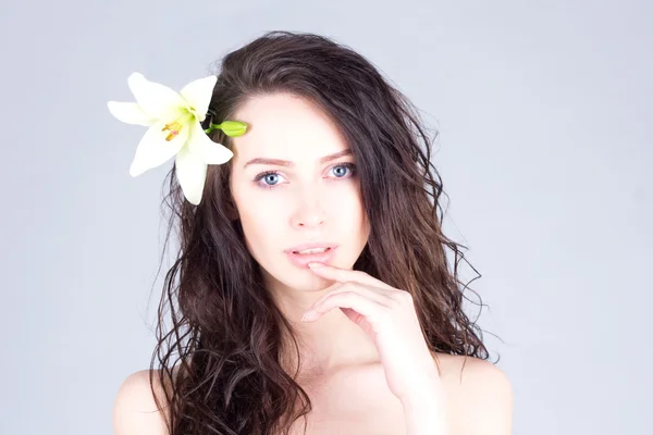 Woman with curly hair and big blue eyes touching lips. Woman with a flower in her hair. Royalty Free Stock Images