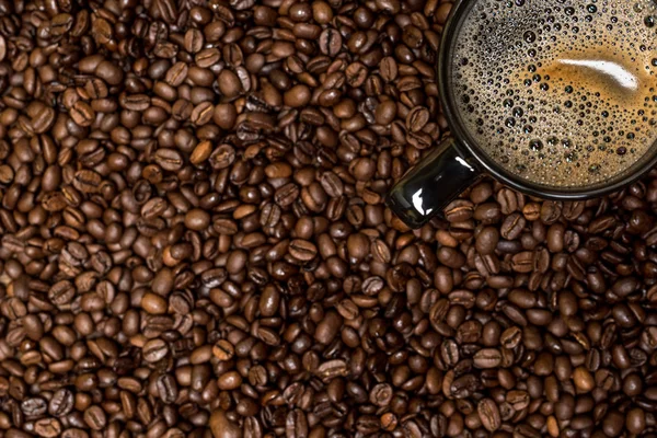 Grãos de café fundo e xícara preta com bebida quente — Fotografia de Stock