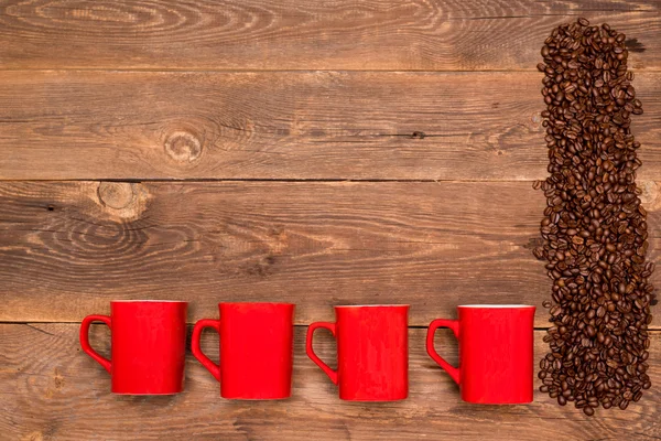 Kahve çekirdekleri ve ahşap masa üzerinde dört kırmızı Kupası — Stok fotoğraf