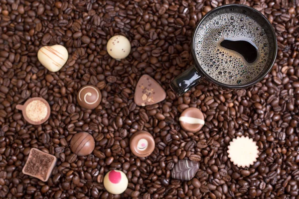 Fundo de grãos de café e xícara preta com pralines — Fotografia de Stock