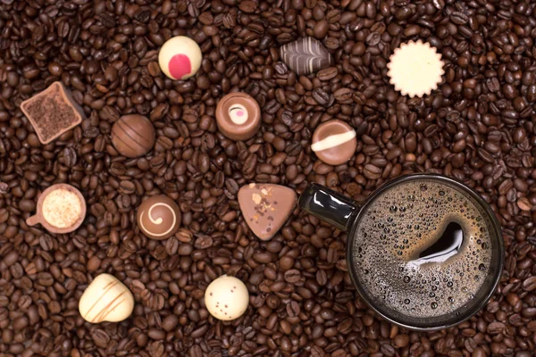 Fundo de grãos de café e xícara preta com pralines — Fotografia de Stock