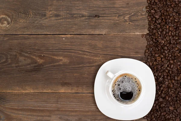 Grãos de café e xícara branca na mesa de madeira — Fotografia de Stock