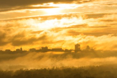 Sis, sis ve turuncu günbatımı bulutlarıyla şehirde gün batımı