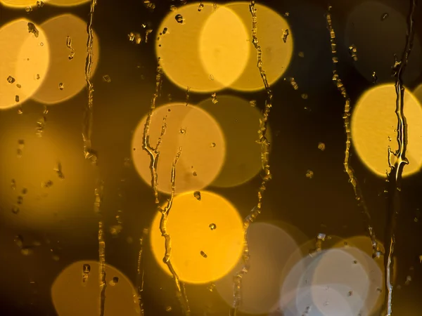 Gotas de lluvia en el cristal de una ventana por la noche — Foto de Stock