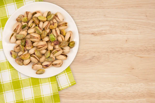 Pistasienøtter i en hvit plate på et trebord. Sett ovenfra – stockfoto