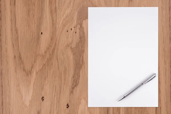 Papel blanco en blanco con pluma sobre un escritorio de madera . — Foto de Stock