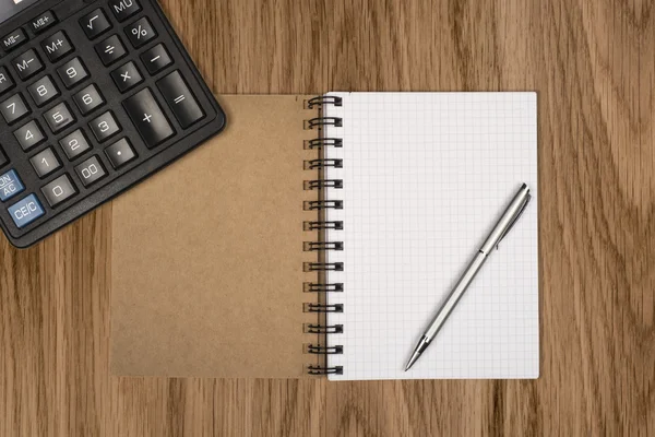 Quaderno, penna a sfera e calcolatrice su scrivania in legno — Foto Stock