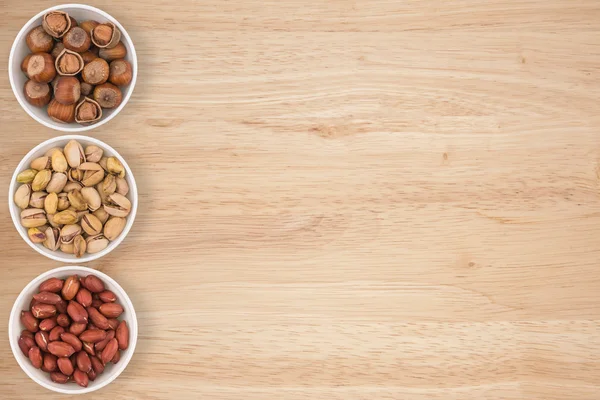 Cacahuètes, noisettes, pistaches dans un bol de cyan sur une table en bois . — Photo