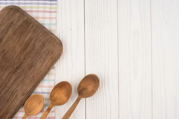 Режущая доска и ложка на кухонной салфетке на старой деревянной доске — стоковое фото