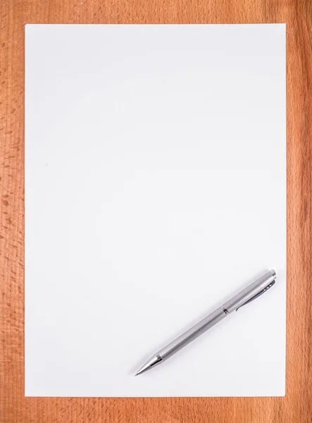 Papel blanco en blanco con pluma sobre un escritorio de madera . — Foto de Stock