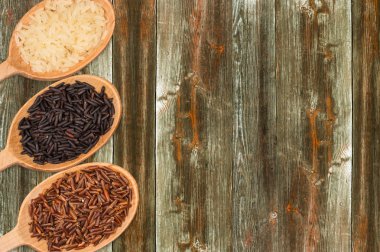 Ahşap bir masa üzerinde bir tahta kaşık kırmızı, beyaz ve siyah pirinç