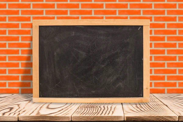 Leeg schoolbord op diagonale houten tafel in rode bakstenen muur, Temp — Stockfoto