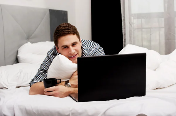 Przypadkowy młody człowiek za pomocą laptopa w łóżku w domu. — Zdjęcie stockowe