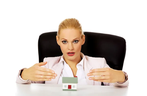 Mujer de negocios sentada detrás del escritorio con modelo de casa —  Fotos de Stock