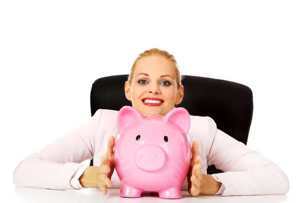 Mujer de negocios feliz con una hucha detrás del escritorio — Foto de Stock