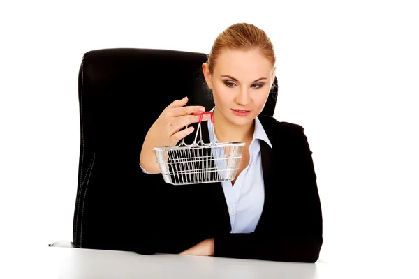 Smile business woman holding shopping cart and sitting behind the desk — Stock Photo, Image