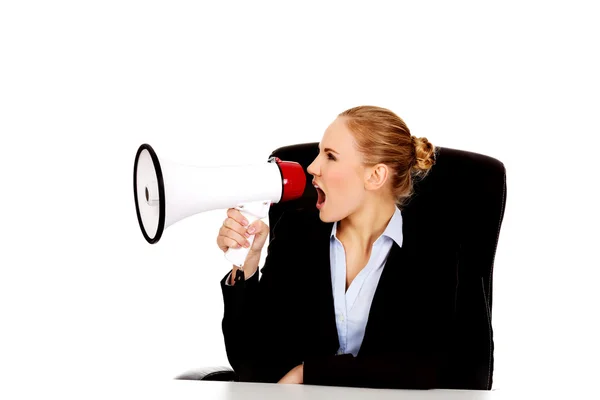 Business woman sitting behind the desk and screaming through a megaphone — Stock Photo, Image