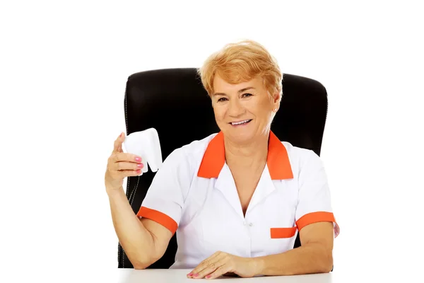 Улыбающаяся пожилая женщина-дантист сидит за столом и держит большую зубную модель — стоковое фото