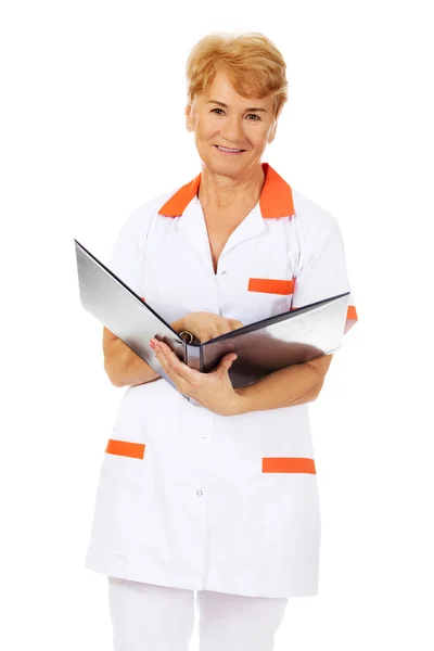 Elderly female doctor or nurse holds black binder and reads — Stock Photo, Image