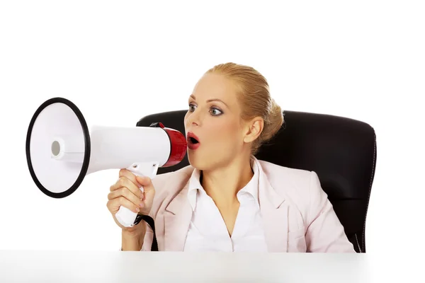 Business woman sitting behind the desk and screaming through a megaphone — Stock Photo, Image