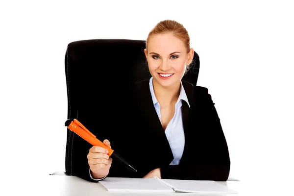 Mujer de negocios sentada detrás del escritorio y escribe algo con una pluma grande —  Fotos de Stock