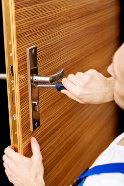 Genç adam tornavidayla kapıyı tamir ediyor.