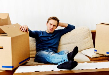 Kanepede karton kutularla oturan yorgun bir adam.