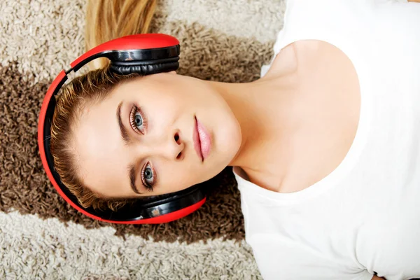 Jovem deitada no tapete e ouvir uma música em fones de ouvido — Fotografia de Stock