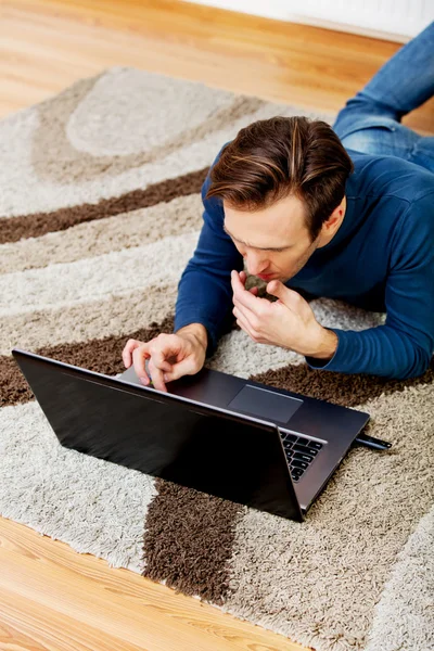 Junger Mann liegt auf dem Boden und benutzt Laptop — Stockfoto