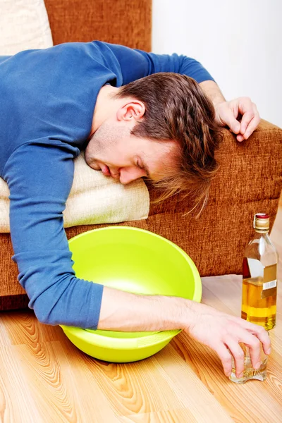 Drunk man sleeping on couch with whikey bottle and bowl — Stock Photo, Image